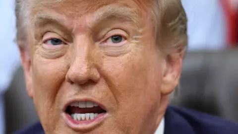 Reuters US President Donald Trump has his mouth open in a close up shot. His eyebrows are raised and he is wearing a blue suit jacket.