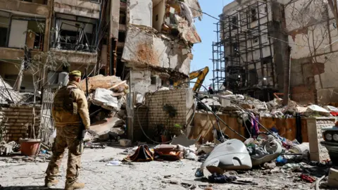 EPA/Shutterstock A Lebanese army soldier stands next to a destroyed residential building the day after an Israeli airstrike in the Ain Mreisseh neighbourhood of Beirut