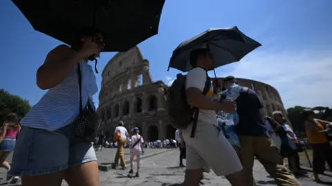 Getty Images People shield themselves from the sun with umbrellas near the Colosseum in Rome