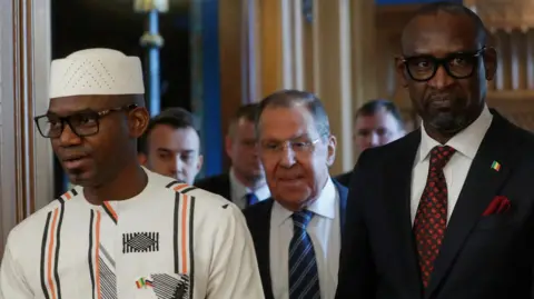 Reuters Malian Defence Minister Sadio Camara, wearing traditional dress, is pictured with Russian Foreign Minister Sergey Lavrov (C) and Malian Foreign Minister Abdoulaye Diop (R), both wearing suits and ties at a meeting in Moscow.