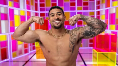 Peacock via Getty Images Sean Reifel seen posing shirtless while flexing his muscles in front of a colorful backdrop as part of a Love Island USA photoshoot. 