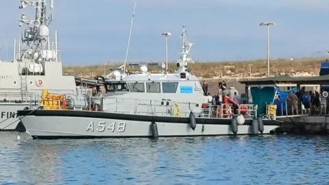 Getty Images Migrants are pictured disembarking from a boat that rescued them after two vessels sank off the coast of Italy's Lampedusa island 