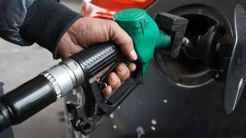 Getty Images A man topping up his car's fuel using a green petrol pump