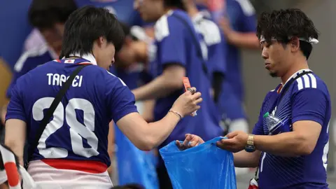 Getty Images Two Japanese football plans cleaning a World Cup stadium and placing their trash in trash bags