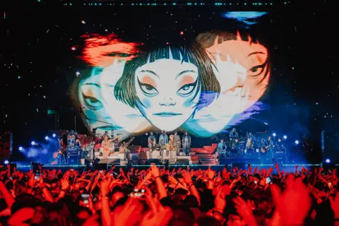 Luke Dyson A shot of Gorillaz stage show in Tottenham, shot from the crowd. Dozens of on-stage musicans are seen underneath a large animated image of a disembodied face