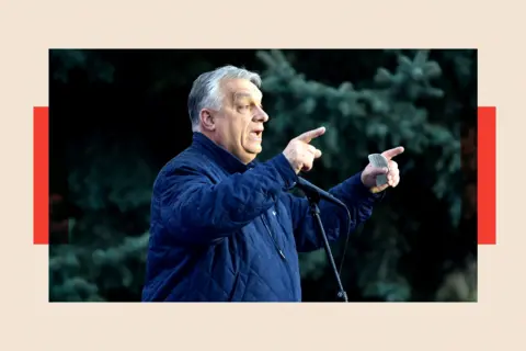 NurPhoto via Getty Images Orban points while standing in front of a microphone. He wears a dark blue casual jacket 