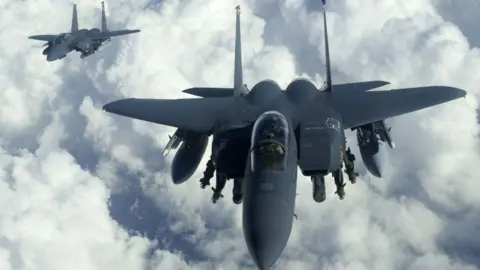 US Air Force via Getty Images Two F-15E Strike Eagle jets soaring through a cloudy sky