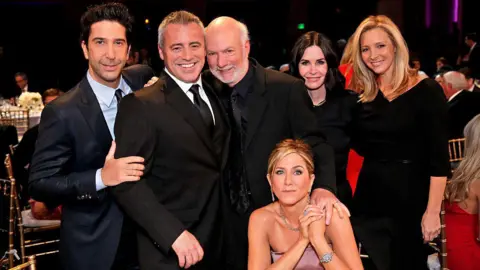 Getty Images Friends actors David Schwimmer, Matt LeBlanc, Courteney Cox and Lisa Kudrow stand and smile with director James Burrows in the centre, who has his hand on the shoulder of a seated Jennifer Aniston, 