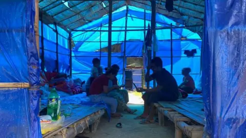 AFP via Getty Images Refugees who fled Myanmar rest in a basic shelter at Farkawn quarantine camp in India's northeastern state of Mizoram near the Myanmar border on September 23, 2021, after they fled across the border following attacks by Myanmar's military on villages in western Chin state. 