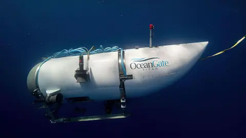PA Media Titan submersible during a dive in the sea. The sub is white with a dome at the front and a tail cover at the back with Oceangate Titan written on its side. 