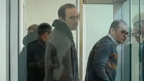 AFP via Getty Images Martin Ryan (centre) looking to his right inside a glass prison cell where there are three other men also inside