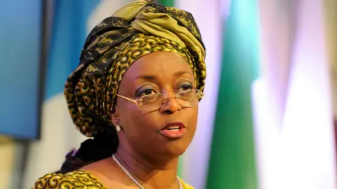Getty Images Headshot of Diezani Alison-Madueke wearing a yellow patterned dress with headdress and glasses.