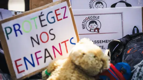 AFP via Getty Images Protesters placed schoolbags on the pavement, along with soft toys and placards bearing the MeTooEcole logo depicting a crying child