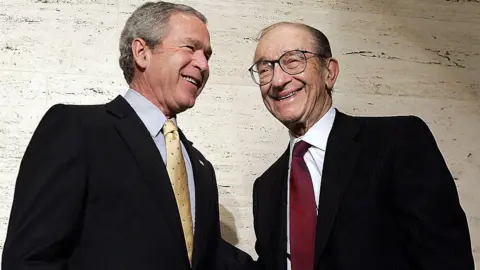 AFP via Getty Images George W. Bush and Alan Greenspan are photographed together. They are smiling and posing for the cameras