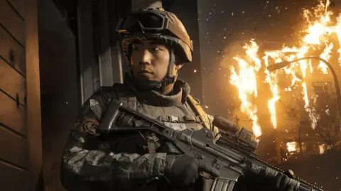 Infinity Ward / Activision An in-game screenshot showing a male Korean soldier holding a gun with a building on fire behind him.