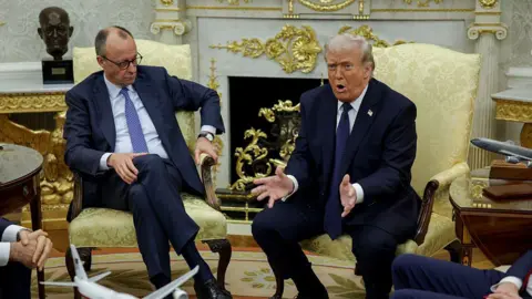Getty Images German Chancellor Friedrich Merz (L) looks at US President Donald Trump (R) as he speaks and gestures with hands outstretched to the media during a meeting in March in the Oval Office of the White House. Both are wearing dark suits and sitting in armchairs.