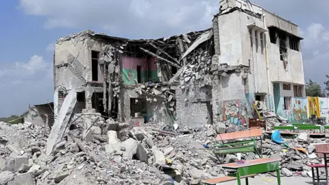 Getty Images A school building partially standing with walls blown off, and rubble all over the ground in front of it