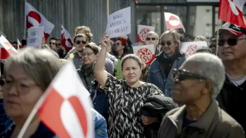 EPA A demonstrator (C) holds a sign that reads 'Make America go away' as others wave flags during a protest outside the US consulate in Nuuk