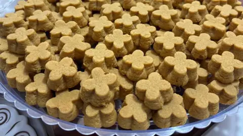 Supplied A close-up image of a plate stacked with small biscuits, each with a distinctive shape like a four-leaf clover.