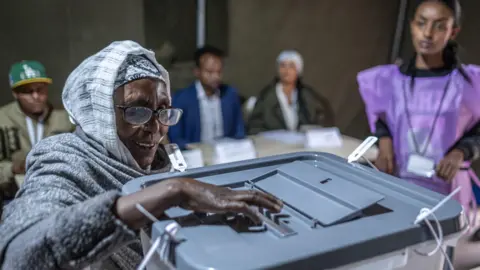 AFP via Getty Images A voter, wearing a grey dress and headscarf and glasses, casts her ballot on a ballot box with a grey cover at Shalla Park polling station in Addis Ababa.