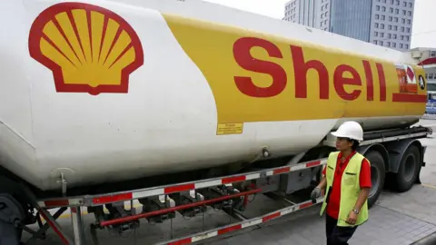 Getty Images A shell branded petrol tanker with a woman wearing a white safety hat and hi-viz vest standing next to it