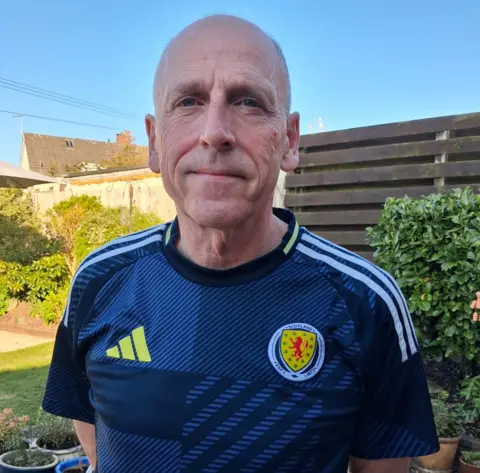 Hamish Husband Hamish Husband, wearing a Scottish football jersey and standing in his garden