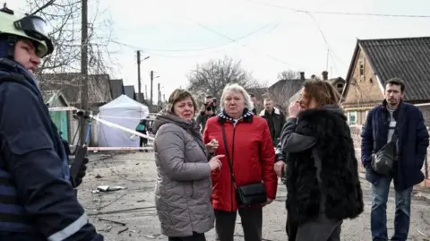Reuters Three women pictured at the scene of the drone strike looking visibly upset. An emergency responder can be seen to their left and another man can be seen on the right. 