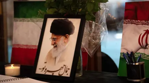 Getty Images A portrait of Iran's Supreme Leader Ayatollah Ali Khamenei is displayed next to Iranian flags, candles and a book of condolences at a mosque in Cape Town