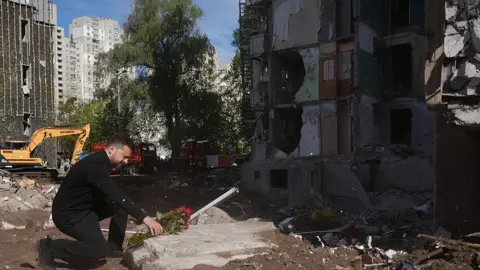 UKRAINIAN PRESIDENCY/HANDOUT Ukrainian President Volodymyr Zelenskyy (L) pays tribute to the victims at the site of a nine-story residential building partially destroyed by a Russian missile strike in Kyiv