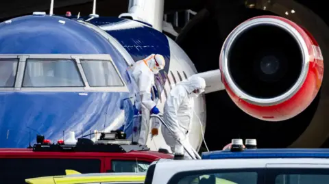 Getty Images People wearing personal protective clothing disembark a plane. 