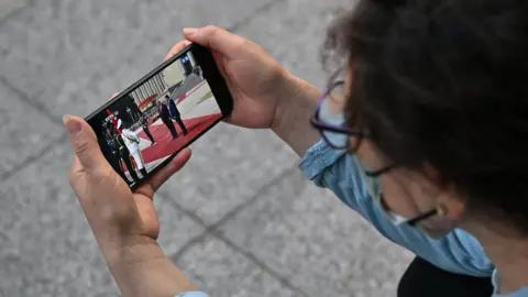 Getty Images A woman watches a video of US President Donald Trump with China's President Xi Jinping on a mobile phone in Beijing, in May this year