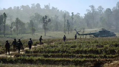 Getty Images In this photo taken on January 24, 2026, soldiers and police walk towards a military Mi-17 helicopter transporting a military-organised press tour at a drug production site southwest of Mongyai, northern Shan State, that was captured by the Myanmar military.