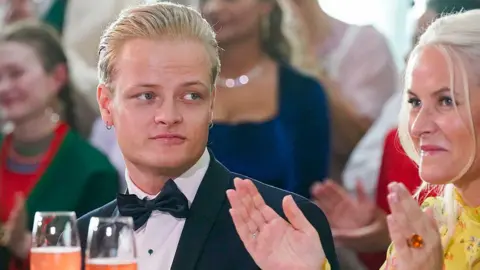 LISE ASERUD/NTB/AFP A young man with blond hair and a bow tie looks on as a woman in a yellow dress claps