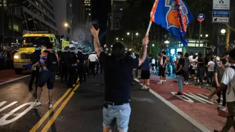 REUTERS/Christian Monterrosa Man walks down a New York street away from the camera holding a Knicks flag with his arms up and a crowd around him