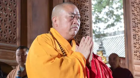 Getty Images Shi Yongxin putting his palms together in a prayer position. He is wearing a yellow robe. File photo
