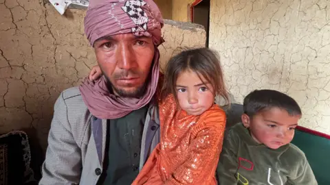 Imogen Anderson/BBC Saeed Ahmad sits with his five-year-old daughter Shaiqa on his lap. His young son is also next to him and stares into the distance 