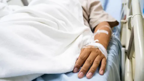 Getty Images A man lies in a hospital bed with tubes inserted in his arm.