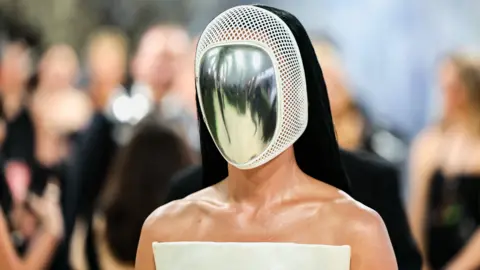 REUTERS/Daniel Cole Katy Perry is seen from the shoulders up. She has on a metal and white mask. She has on a white top with bare shoulders and she has long black hair