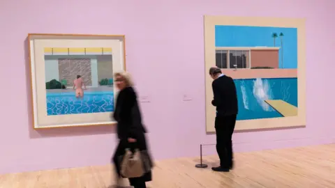 Getty Images Two museum goers walk past the swimming pool paintings of David Hockney
