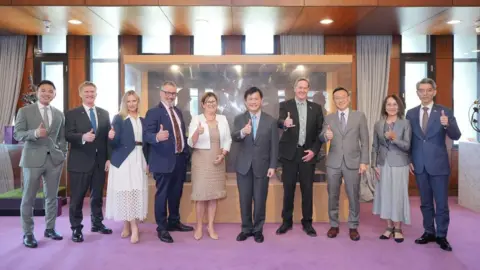 Lin Chia-lung/Facebook A row of men and women in formal attire flashing the thumbs-up sign to the camera.