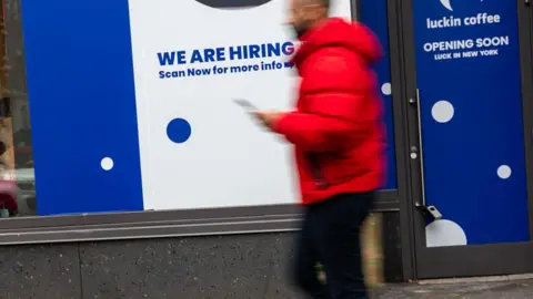Getty Images A 'now hiring' sign is displayed in a business's window in Manhattan on January 09, 2026, in New York City.