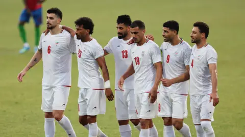 Reuters Members of the Iranian football squad are pictured walking on the pitch in a white football kit, at a friendly match in Turkey on 29 May 2026.