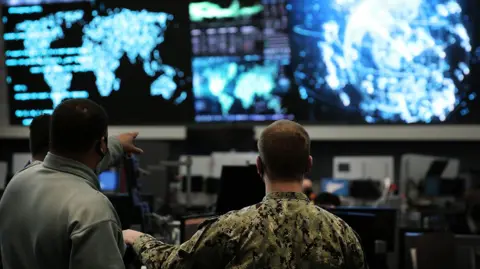 Josef Cole, ALSSA Two us cyber command officers in front of giant screens with data and information on them