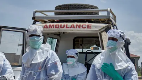 Reuters Three healthcare workers are pictured in front of an ambulance, wearing masks, gloves and other protective gear