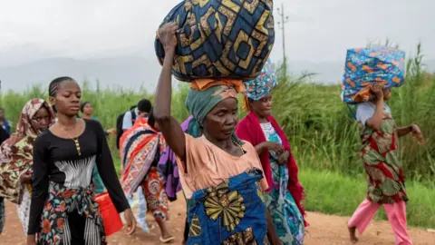 Reuters Women - described by Reuters as foreigners - walk on a road with their belongings after rebels seized Uvira city in December