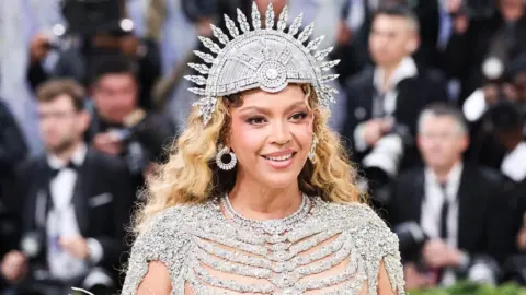 EPA US performer Beyonce poses on the red carpet for the 2026 Met Gala wearing a shimmering skeletal gown and a spherical headpiece as photographers in suits stand behind her.