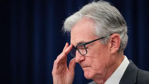 Getty Images Outgoing Federal Reserve chair Jerome Powell wearing a white shirt and dark suit jacket readjusts his glasses while speaking to the press.