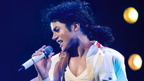 Universal Jaafar Jackson, wearing white and holding a microphone, performing as Michael Jackson in the musical biopic Michael