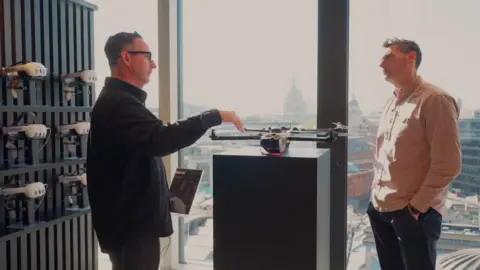 Joe Tidy and Richard Drake in the Anduril London HQ standing in front of a drone