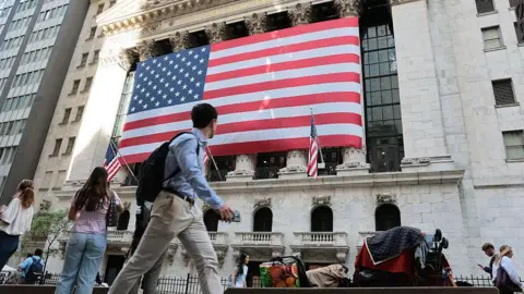 Getty Images The New York Stock Exchange is seen during morning trading on May 26, 2026. A large American flag hangs from the front of the building and people walk in the street in front of it